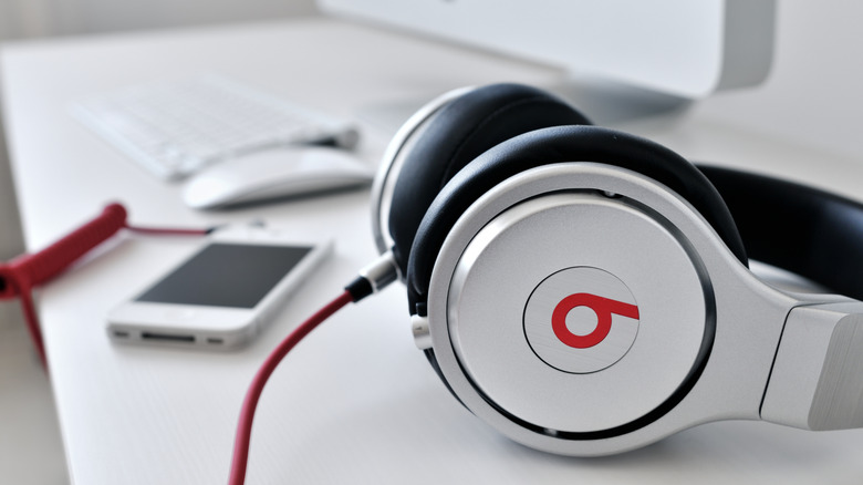 A pair of original Beats headphones sitting on a desk with a phone and computer in the background.