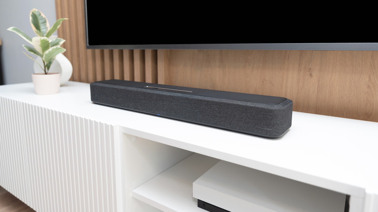 A sleek soundbar sitting on a wooden entertainment console underneath a flat-screen TV.