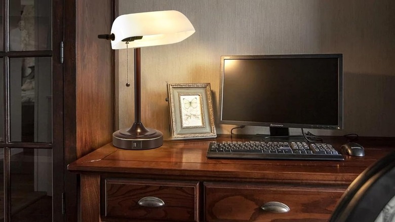 A classic green banker's lamp with a gold base illuminating an office desk.