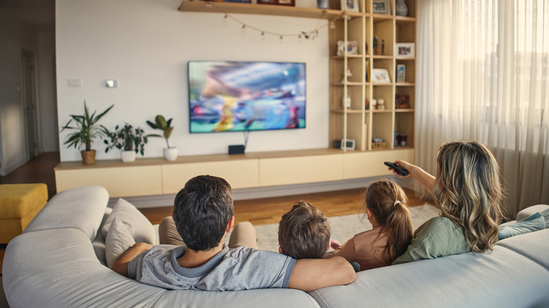 A family sitting together on a couch watching a bright, clear television in a modern living room.