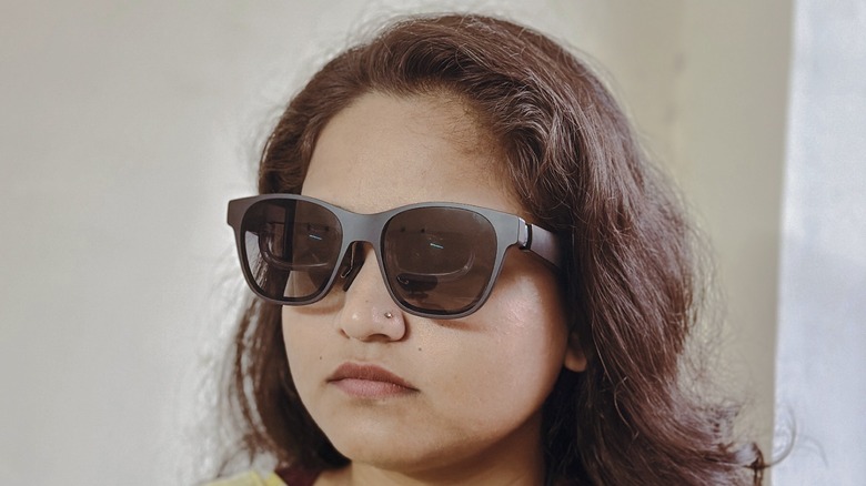 Profile view of a user wearing slim AR glasses, showing the tethered USB-C cable connection.