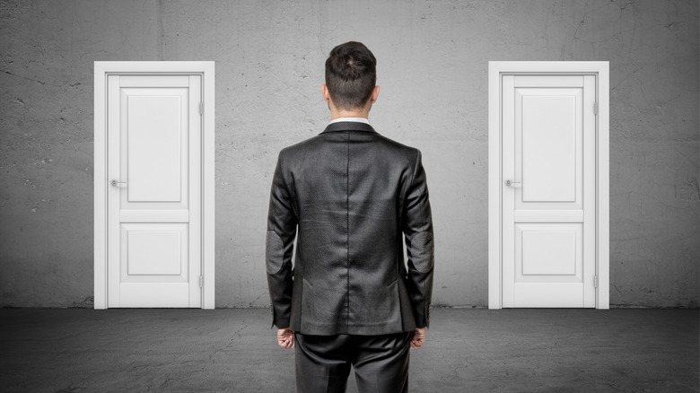A man in a suit standing before two identical white doors.