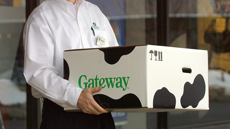 An employee holding a large Gateway computer box featuring the brand's iconic cow-print design.