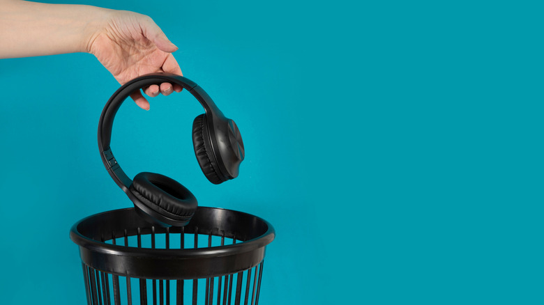 A hand dropping a pair of headphones into a trash bin.