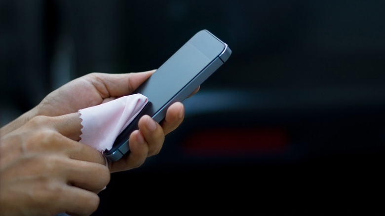 Close-up of a hand cleaning a smartphone display with a microfiber cloth.