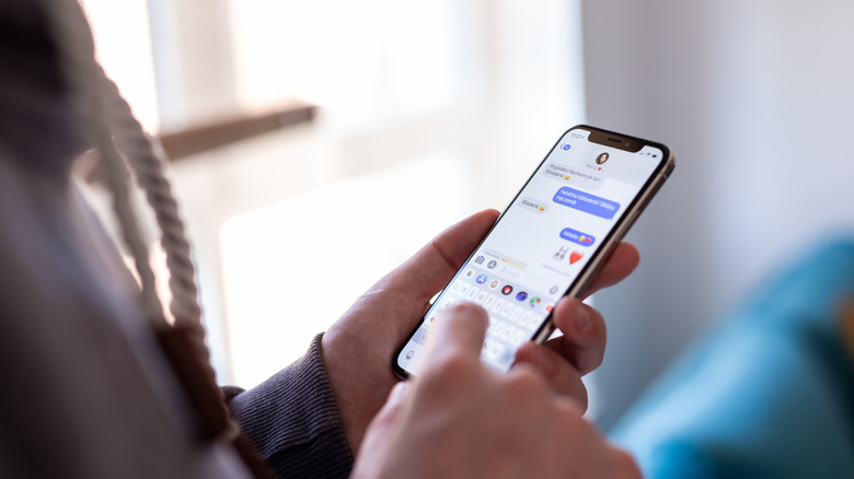 A user's hands typing a message on an iPhone screen within the iMessage app.