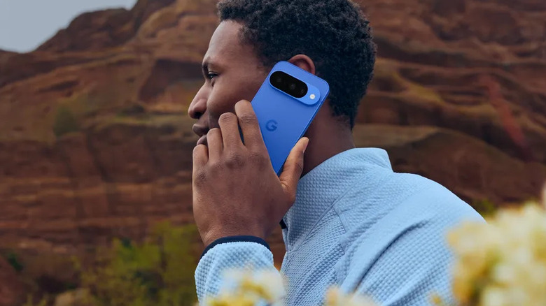 A person using the Google Pixel 10 Pro outdoors with a red rock cliff background.