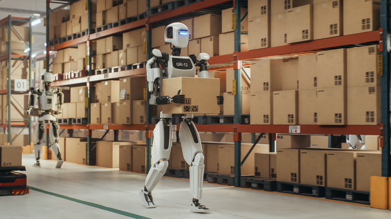 A robotic worker walking with a cardboard box inside a smart factory warehouse.