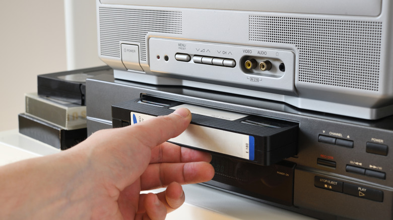 Close-up of a person's hand inserting a black VHS cassette into a player.