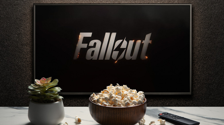 A television screen displaying the Fallout logo with a remote and bowl of popcorn in the foreground, representing the Amazon Prime Video viewing experience.