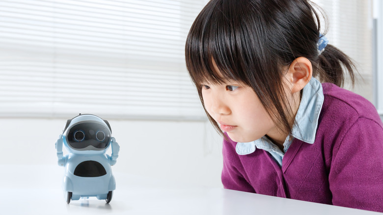 A young girl interacting closely with a small educational robot.