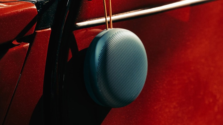 A Bang & Olufsen Beosound A1 speaker hanging against a vibrant red texture.