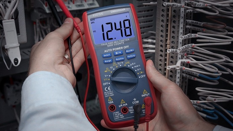 A person holding an AstroAI Digital Multimeter to test electrical voltage.