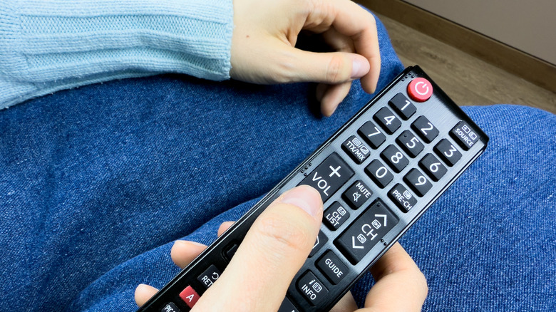 Close-up of a person's hand holding a Samsung Smart Remote pointed toward a television.