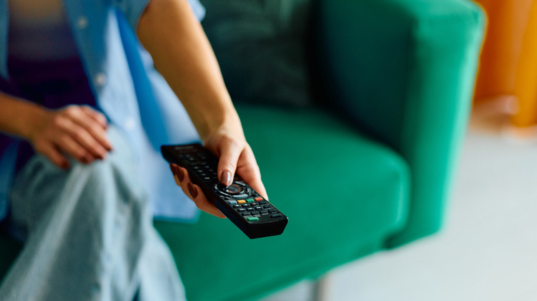 A person holding a black television remote control toward a screen.