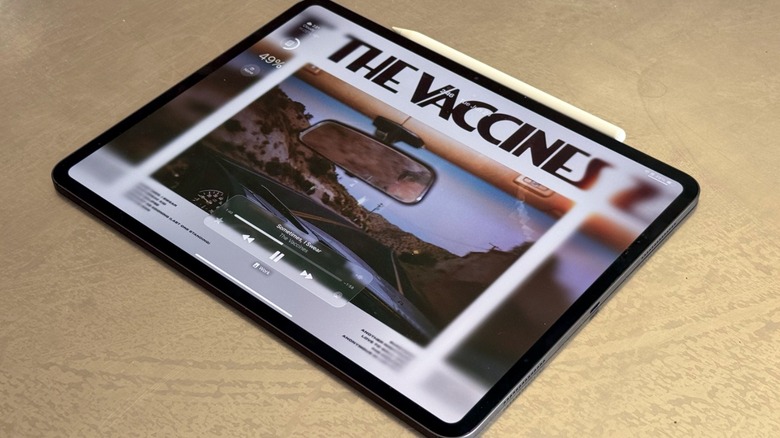An iPad Pro displaying the iPadOS 26 lock screen with deep blacks and vibrant colors.
