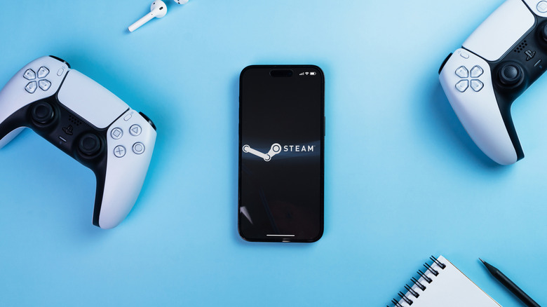 An Android phone with the Steam logo placed on a table next to gaming controllers.