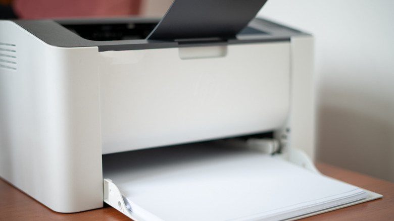 An old white inkjet printer sitting on a brown wooden table.