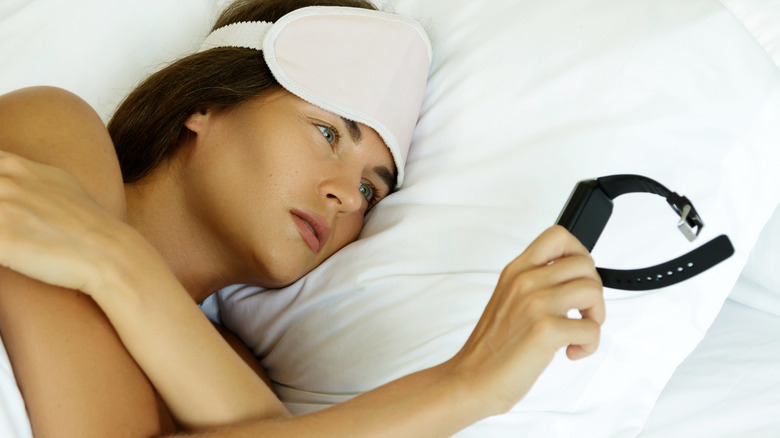 A person in bed checking their smartwatch to review their sleep stages.