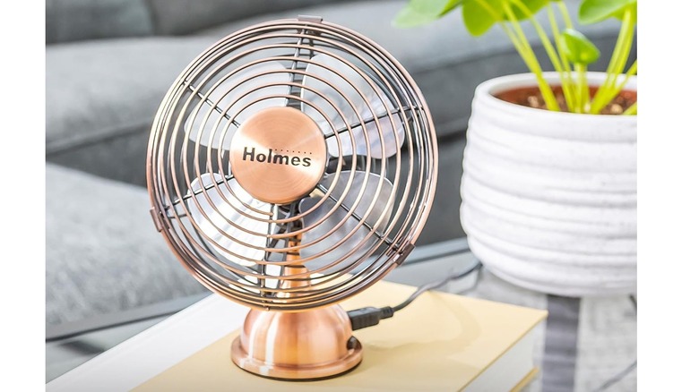 A Holmes 4-inch mini desk fan with a metallic vintage finish sitting next to a potted plant.