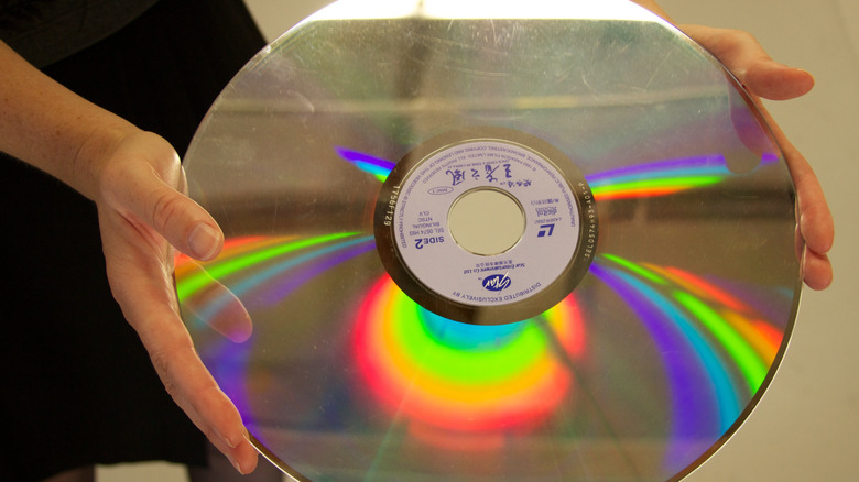 Hands holding a large LaserDisc reflecting rainbow light on its surface.