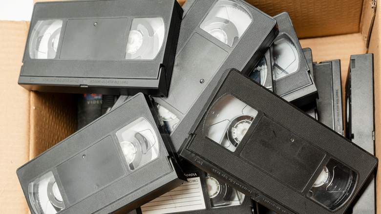 A cardboard box filled with various unsorted VHS tapes.