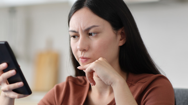 A woman looking at her smartphone screen with a mildly frustrated expression.
