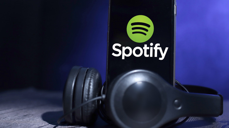 An Android phone showing the Spotify logo next to a pair of headphones on a flat surface.