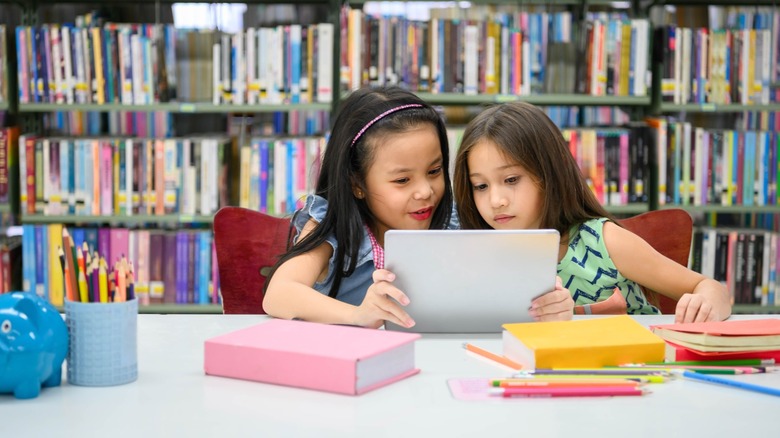 Two children sitting together looking at a tablet screen.
