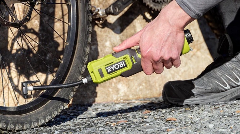 A person using the Ryobi 4V high-pressure inflator to check and fill a car tire.