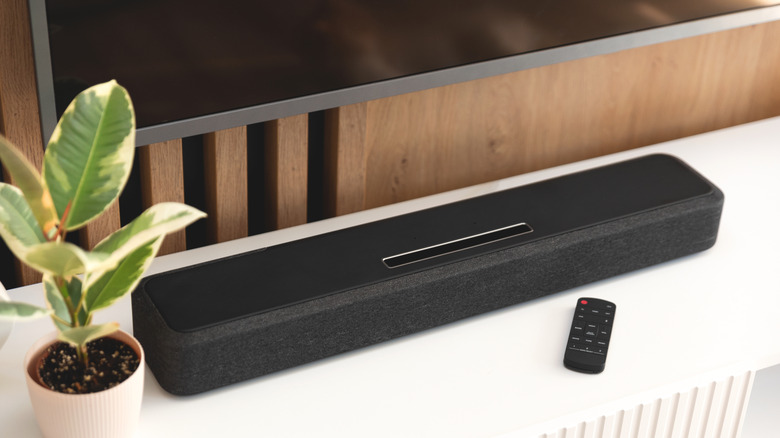 A sleek black soundbar positioned on a wooden TV stand below a flat-screen television.