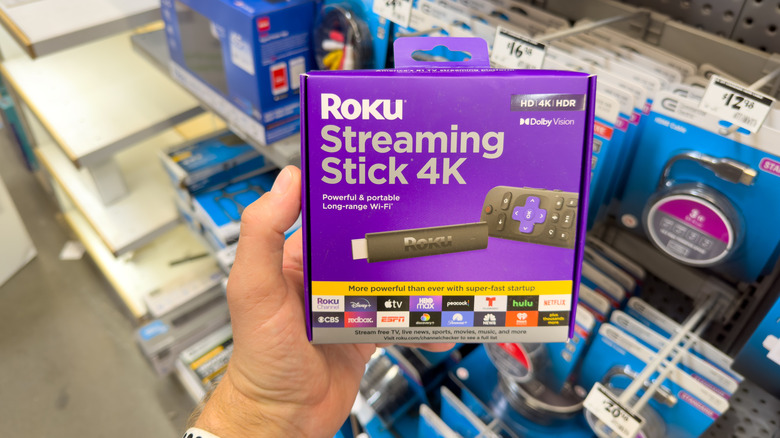 A person holding a Roku Streaming Stick 4K box in a retail store environment.
