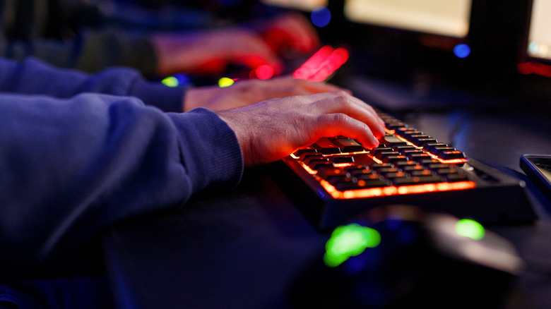 Top-down view of a person's hands over a backlit RGB mechanical gaming keyboard.