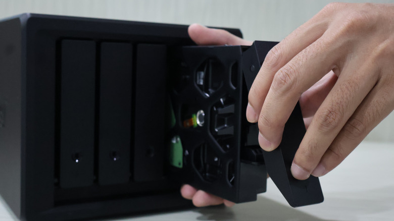 A person inserting a hard drive into a network attached storage unit.