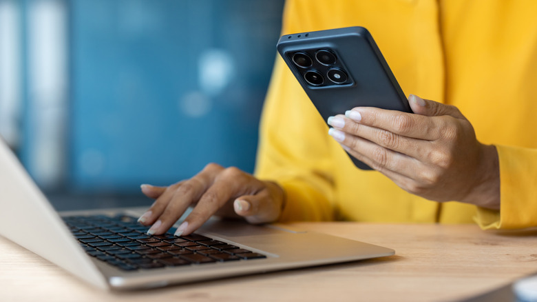 A person holding a smartphone while working on a laptop, symbolizing data tethering and connectivity.
