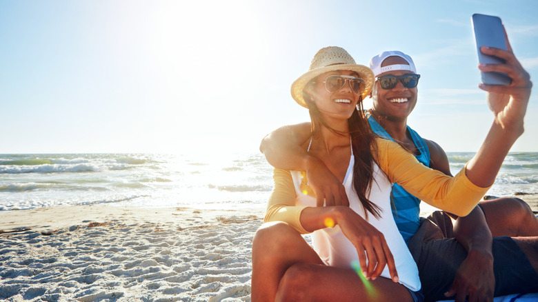 A couple taking a selfie on a sunny beach with a smartphone.