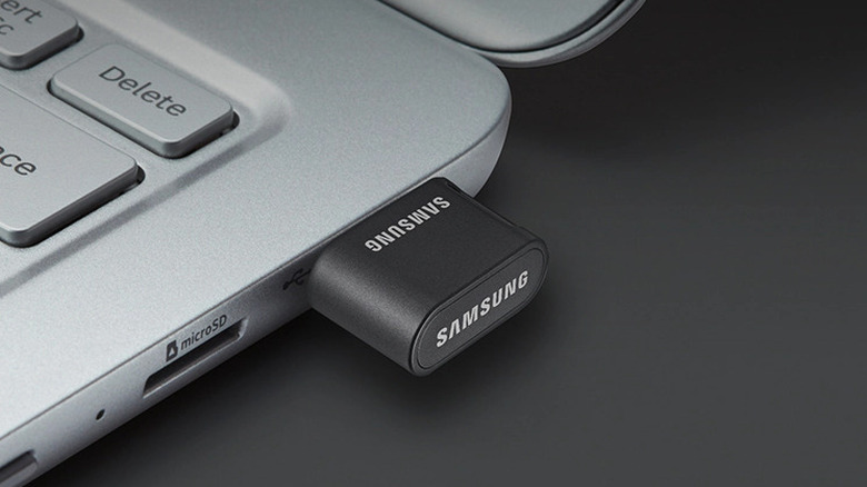 A black Samsung USB flash drive plugged into the port of a modern laptop.