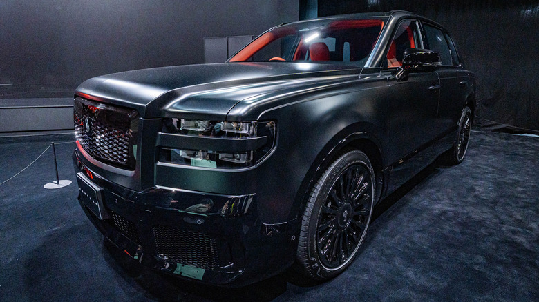 A dark green Toyota Century SUV on display at a motor show under bright lights.
