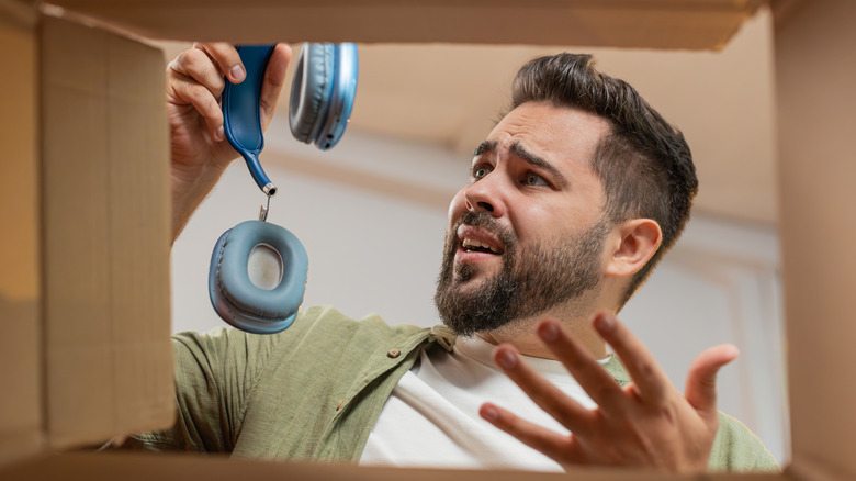A man looking disappointed and frustrated while holding a pair of headphones.