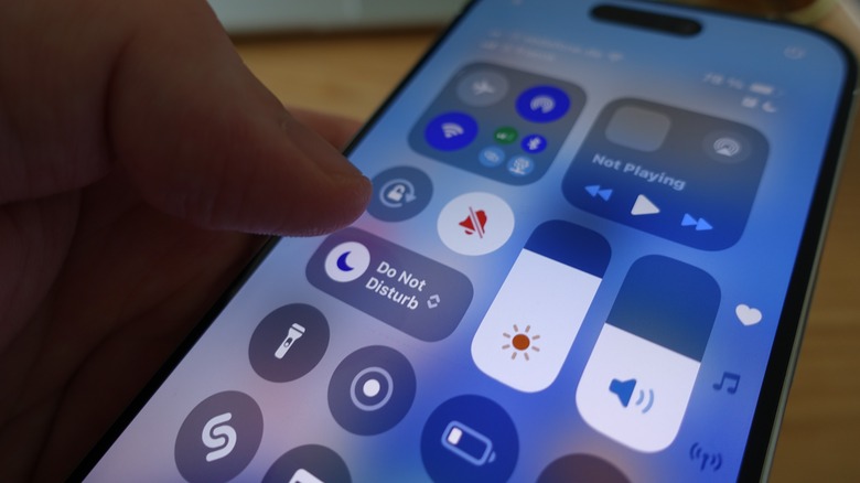 A hand using an iPhone's Control Center to access system toggles.
