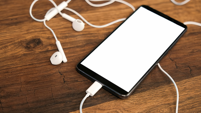 A smartphone resting on a wooden table connected to earphones via its USB-C port.