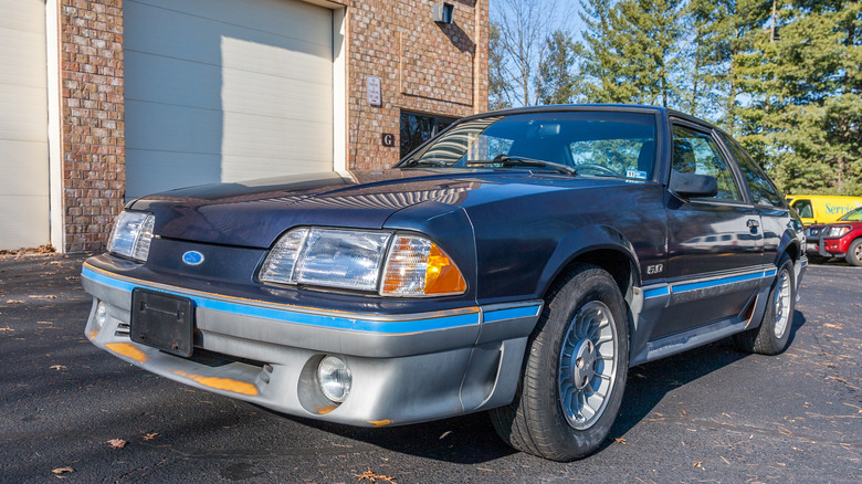 A Fox Body Mustang GT parked in an urban parking lot setting.