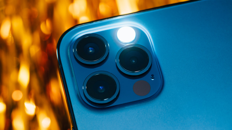 Close-up of the iPhone 12 camera lenses with the LED flashlight brightly illuminated.