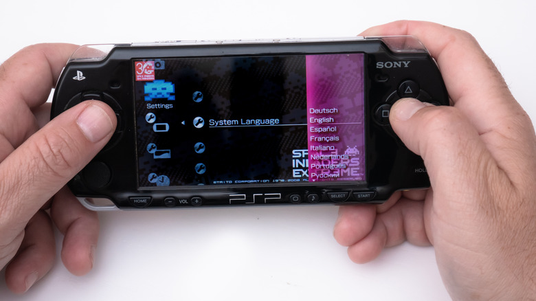 A person holding a PSP and navigating the settings menu.