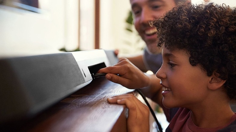 A person plugging a high-speed HDMI cable into the back of a soundbar unit.