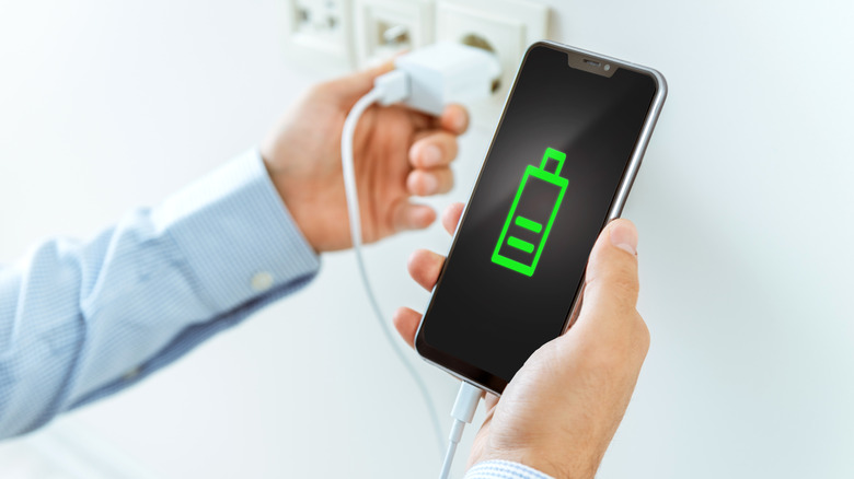 A person connecting a charger to a phone, illustrating the daily impact of fast charging battery health and cycle longevity.