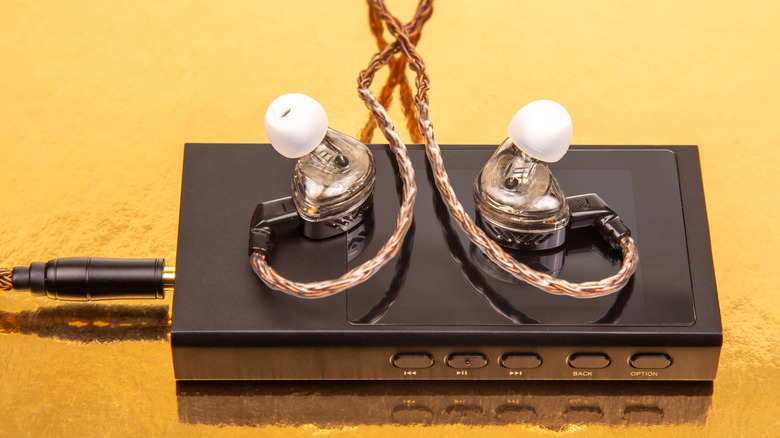 A portable DAC and high-quality In-Ear Monitors resting on a bright yellow background.