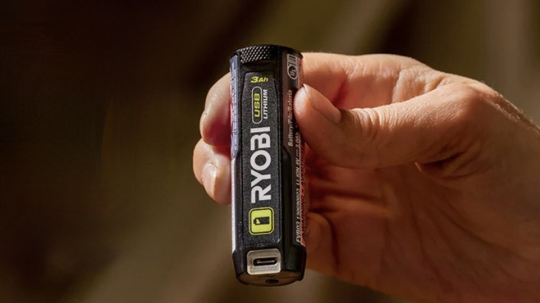 A close-up of a person holding the compact Ryobi 4V USB Lithium battery pack.