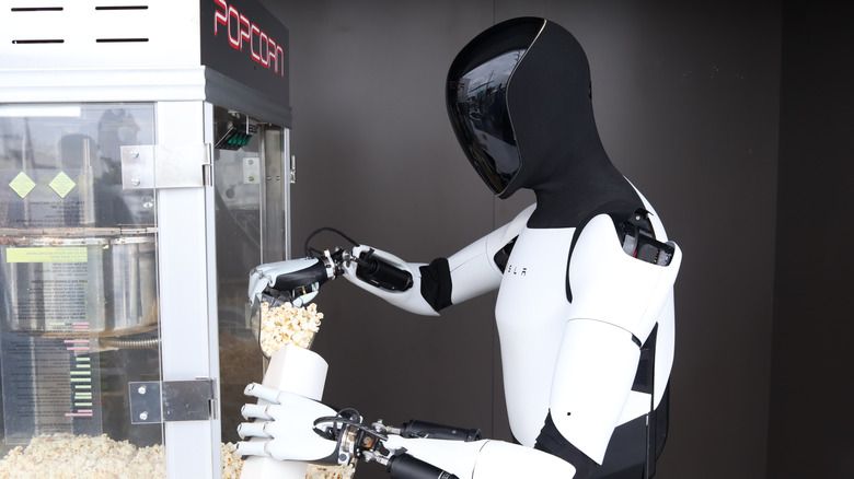A Tesla Optimus humanoid robot serving popcorn to people at a public venue.