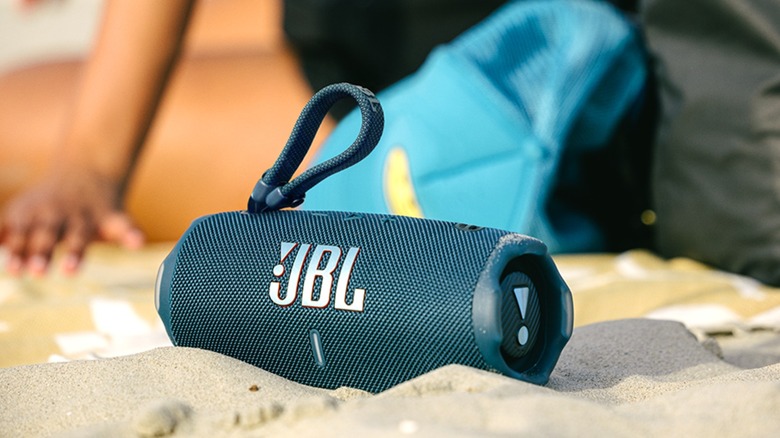 A JBL Charge 6 speaker resting on sandy ground.